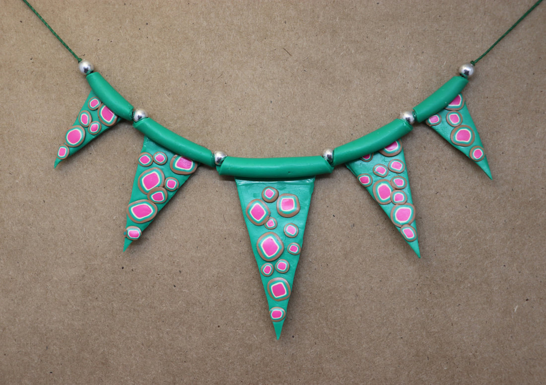 A string of green beads with green, white, pink, and brown polka dots. They are triangles and resemble bunting. 