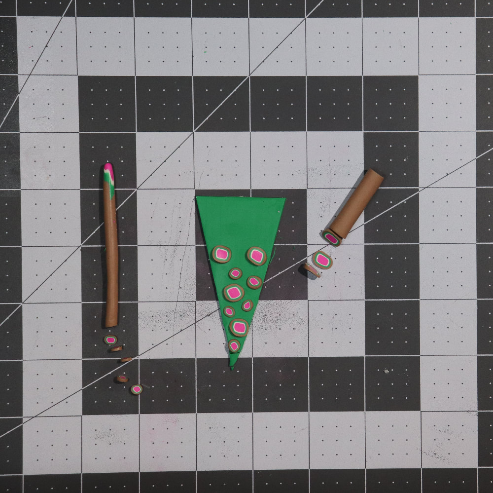 The same green triangle with more dots on it. These are smaller in size. There are also two canes (tubes of patterned clay) on each side with slices cut out. 