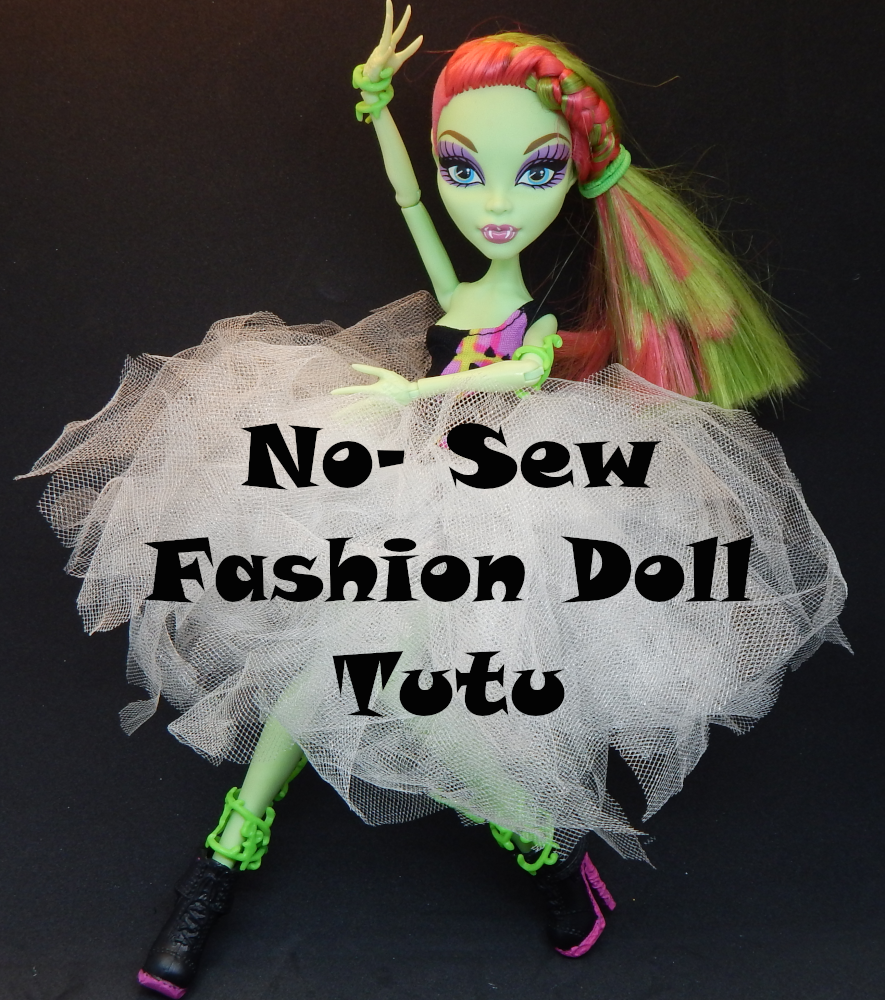 A Picture of a green skinned fashion doll with pink and green hair. she is holding her arms in a ballet like pose and wearing a tutu made of white tulle. Text across the tutu reads 