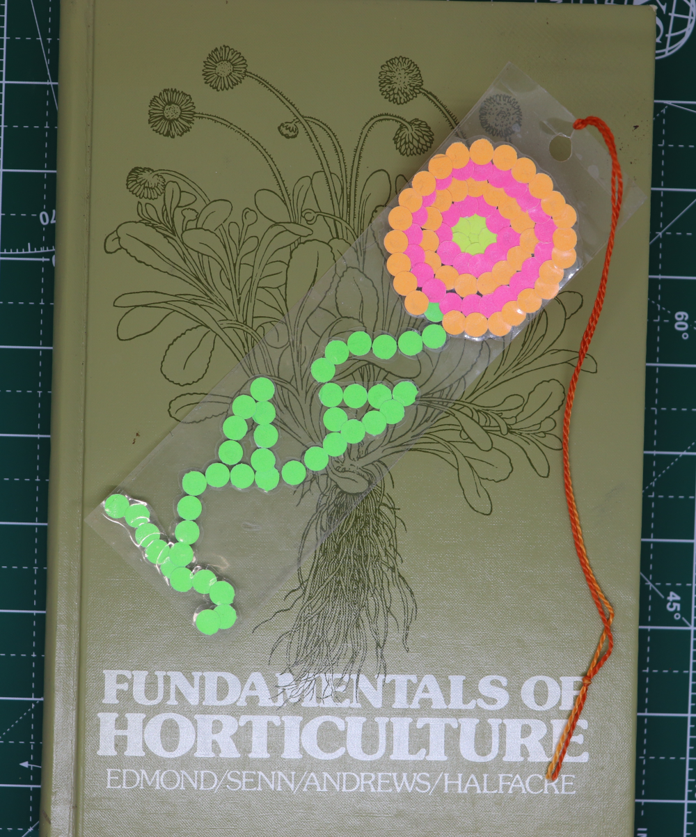 A bookmark with a flower made out of different colored paper dots rests on top of a book