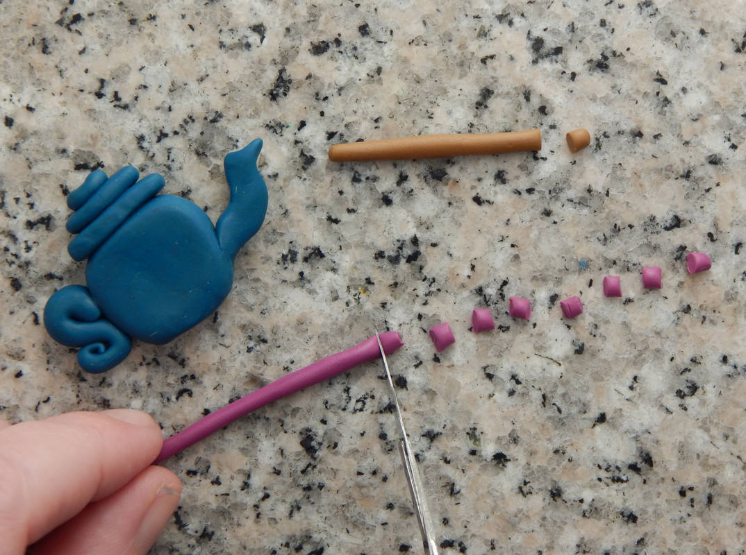 A snake of brown clay and pink clay being cut into very small pieces. The blue teapot bead is in the corner. 