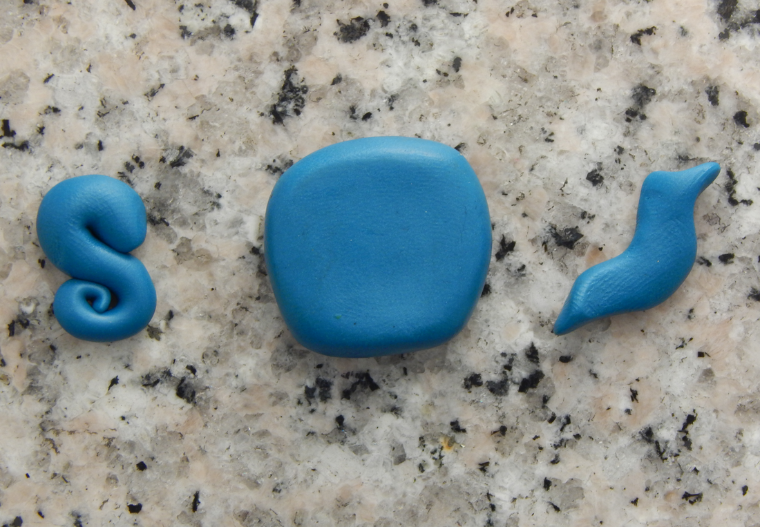 Three pieces of blue clay laid out on a grey speckled background. One is curved into a S shape with spirals, one is a flattened square with rounded corners, and one is a teapot spout shape