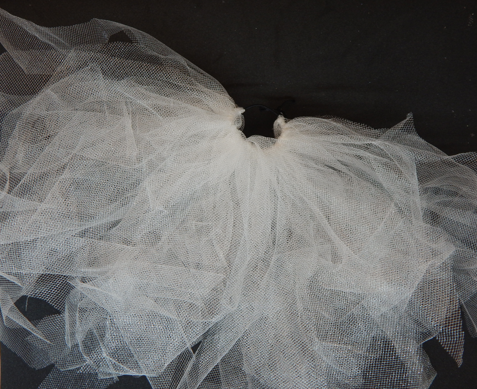 Multiple pieces of white tulle are attached to a black elastic band. It is about halfway covered.