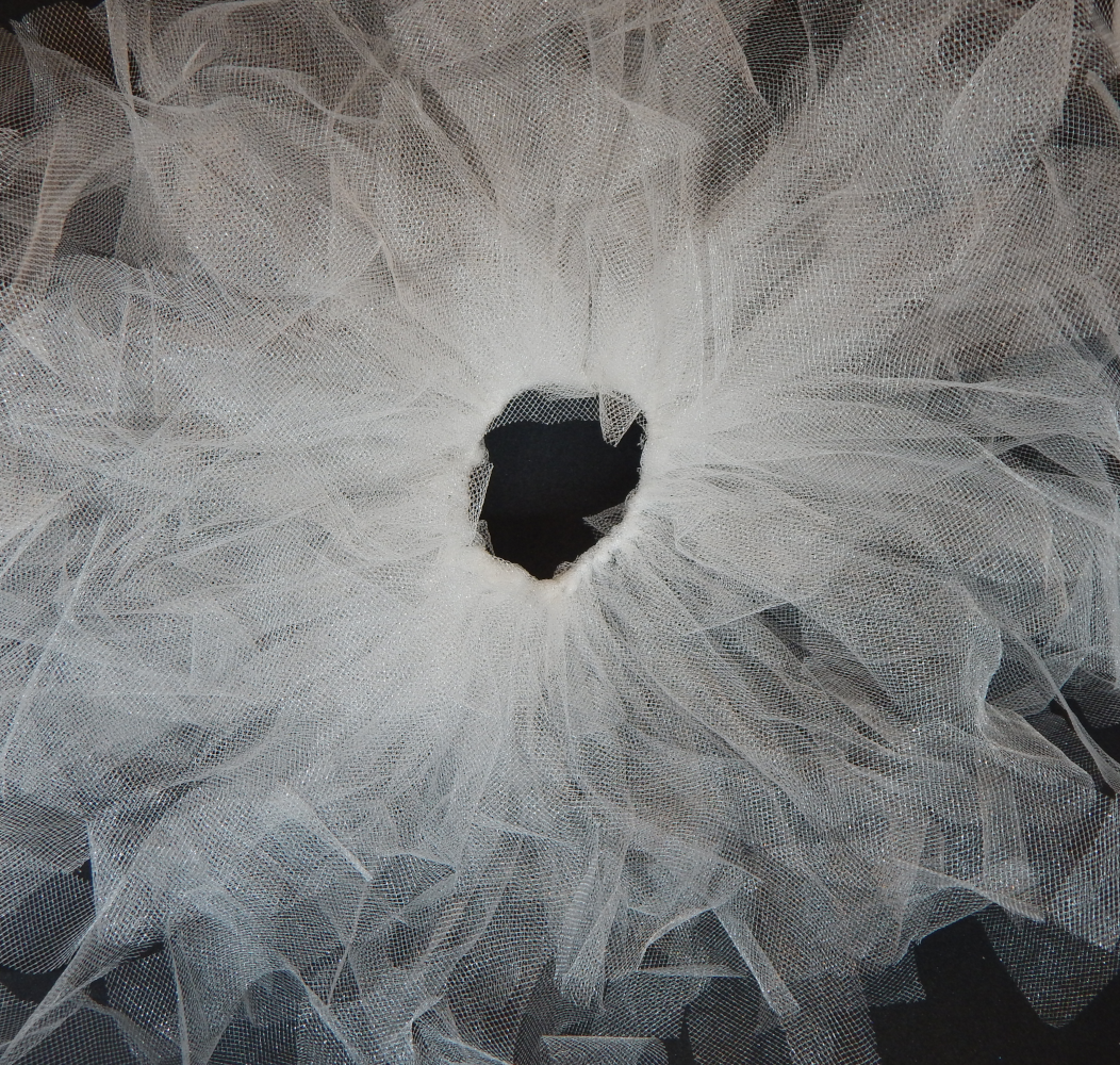 A picture of multiple tulle pieces attached to a black elastic band, covering the band completely leaving a circle of black and fanning out from it 