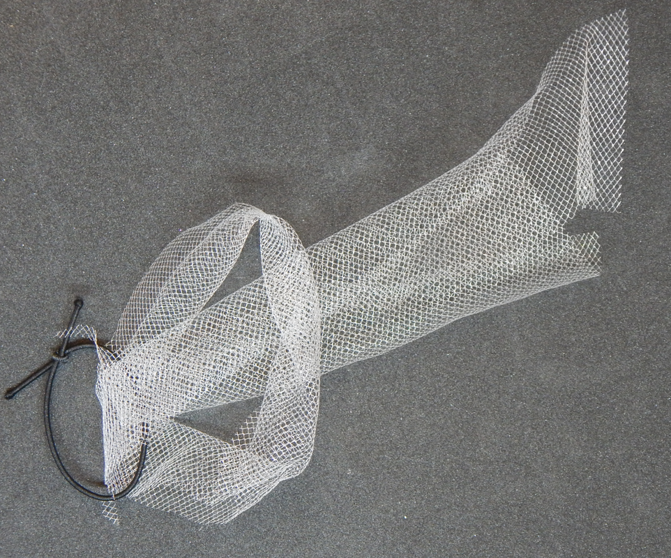 A piece of white till wrapped around a black elastic band, partway through the process of tying a lark's head knot. The two loose ends of the tulle are pulled through the loop made by folding the strip in half.