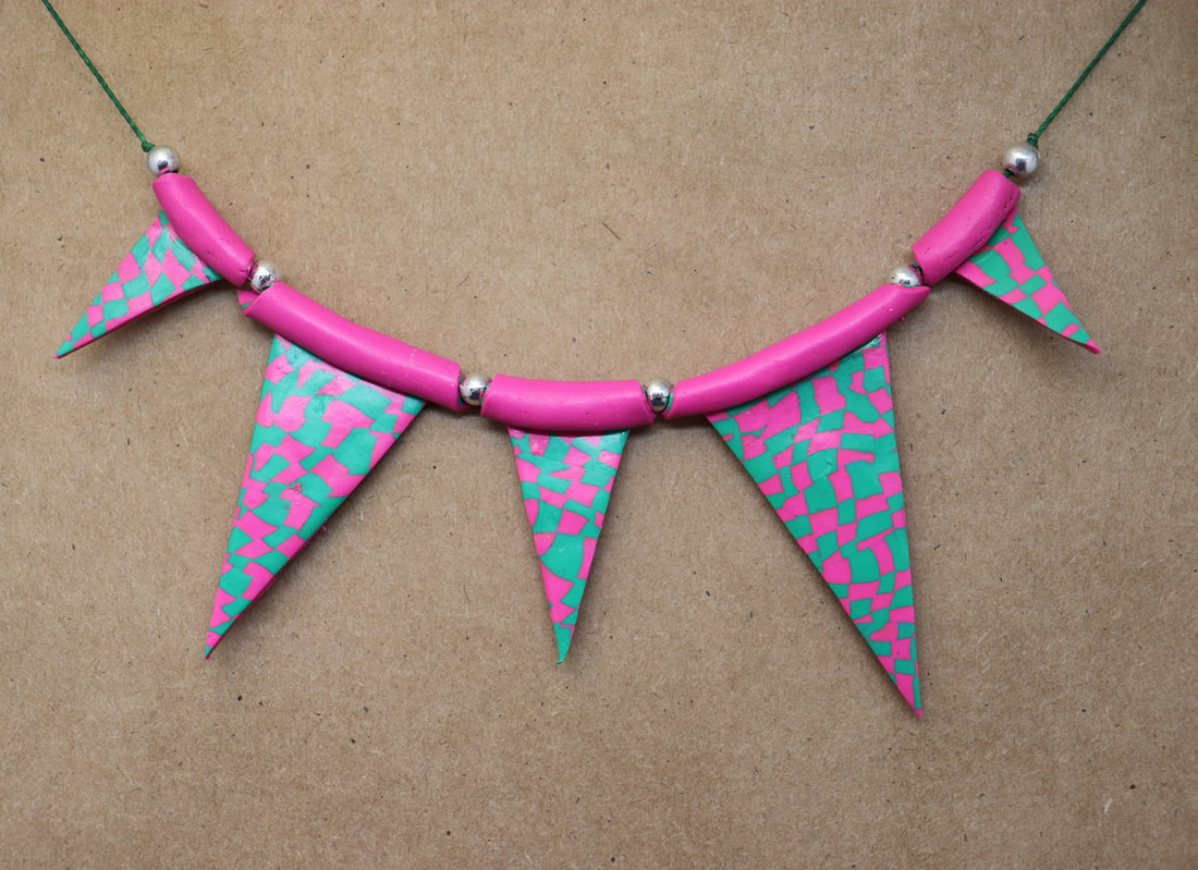 A string of triangle beads in green and pink checkerboard. They are strung with a round silver colored bead in betwwen them and resemble a string of bunting. 