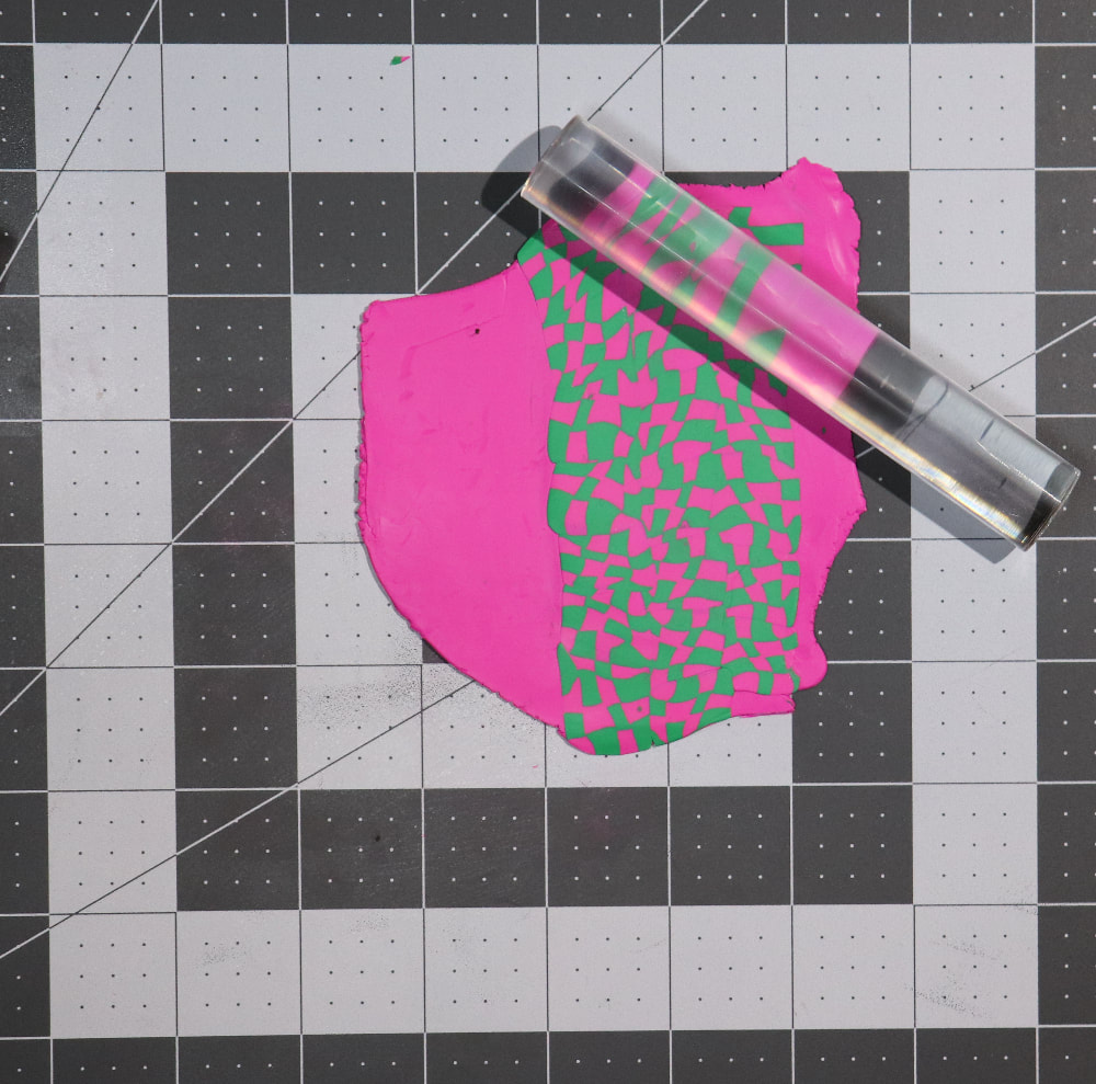 The decorated pink sheet of clay with a clear acrylic roller smoothing the checkerboard design out. 