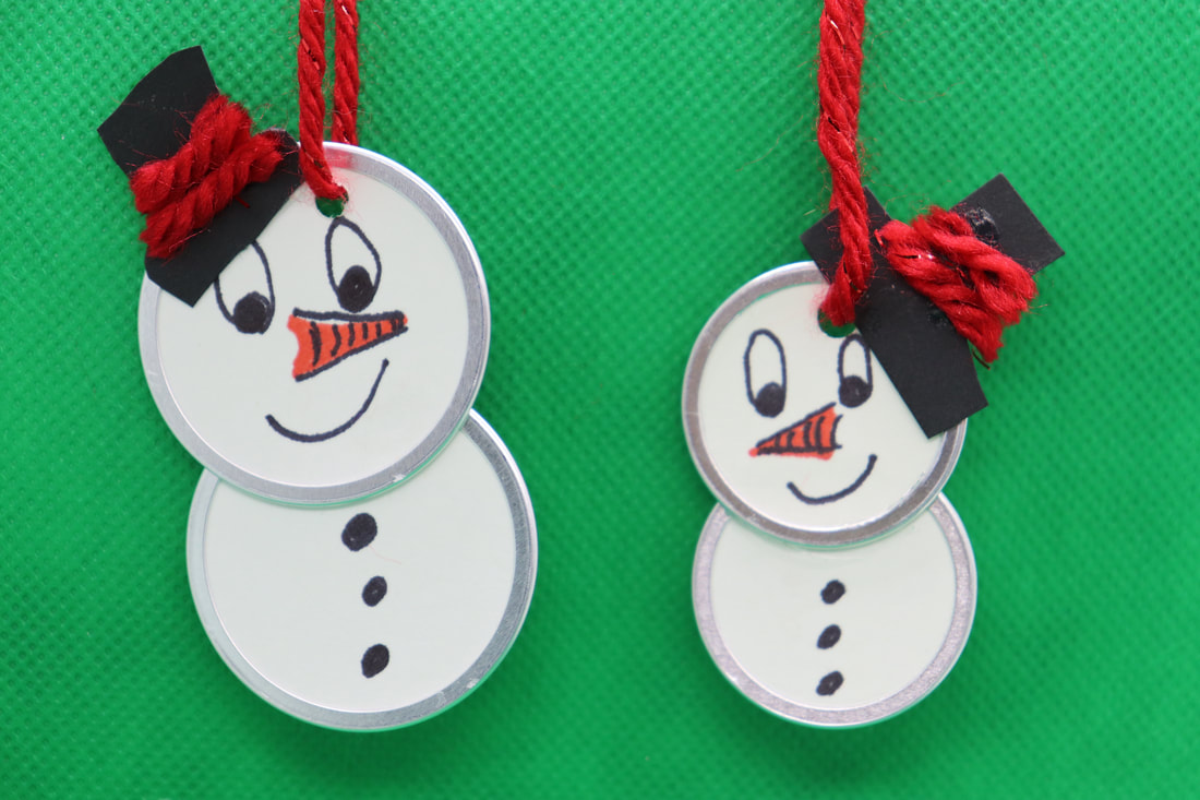 Two snow people ornaments on a green background. They have a smiling face with a drawn carrot nose, and black hats tilted with a red yarn accent.