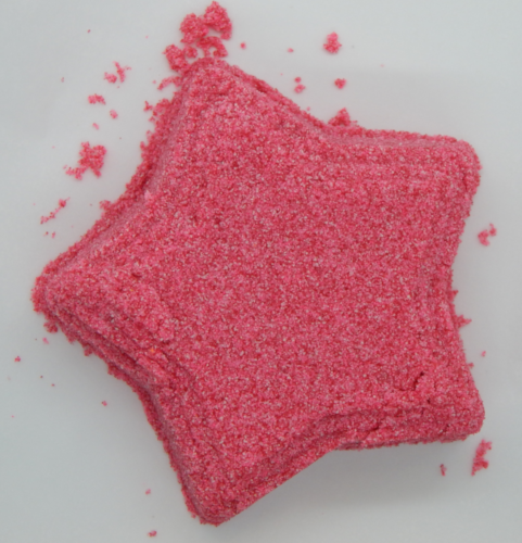 A dark pink star made up of granular sand like material, tilted slightly to the left on a white background.