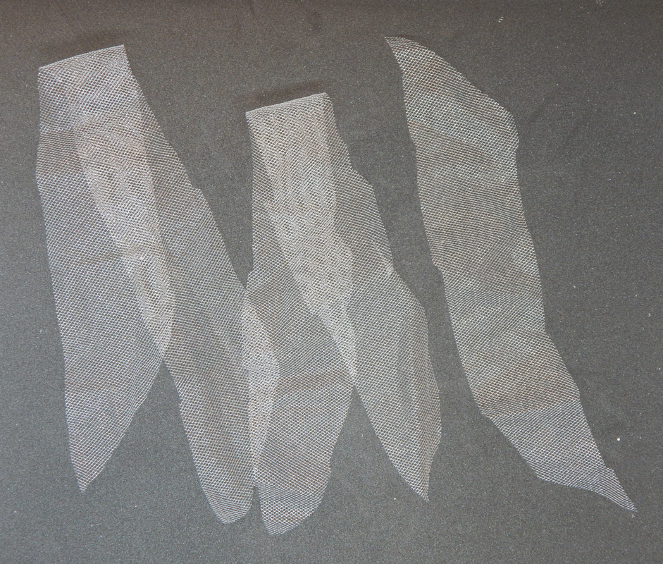 A picture of three strips of white tulle on a black background. Two of them are folded in half