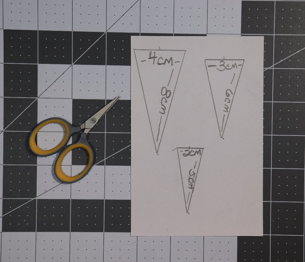 A cutting mat with an index card and scissors on it. There are triangles drawn on the index card.