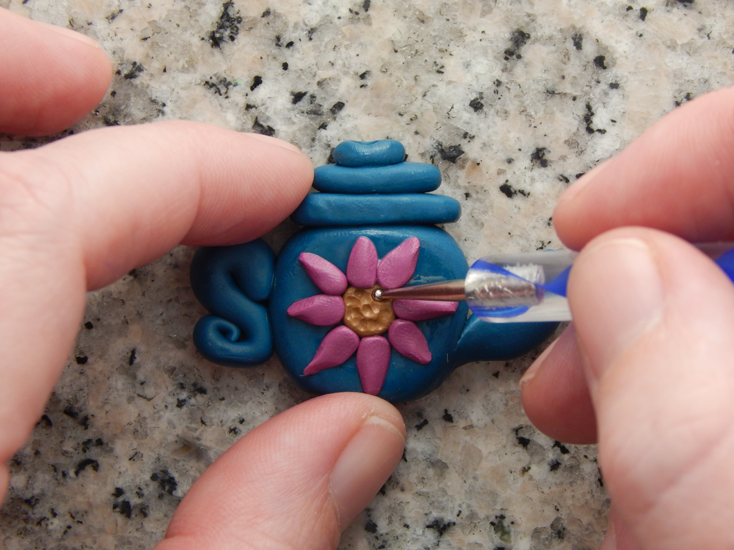 One hand holds the teapot bead while the other uses an embossing tool to press small circles into the flower center. 